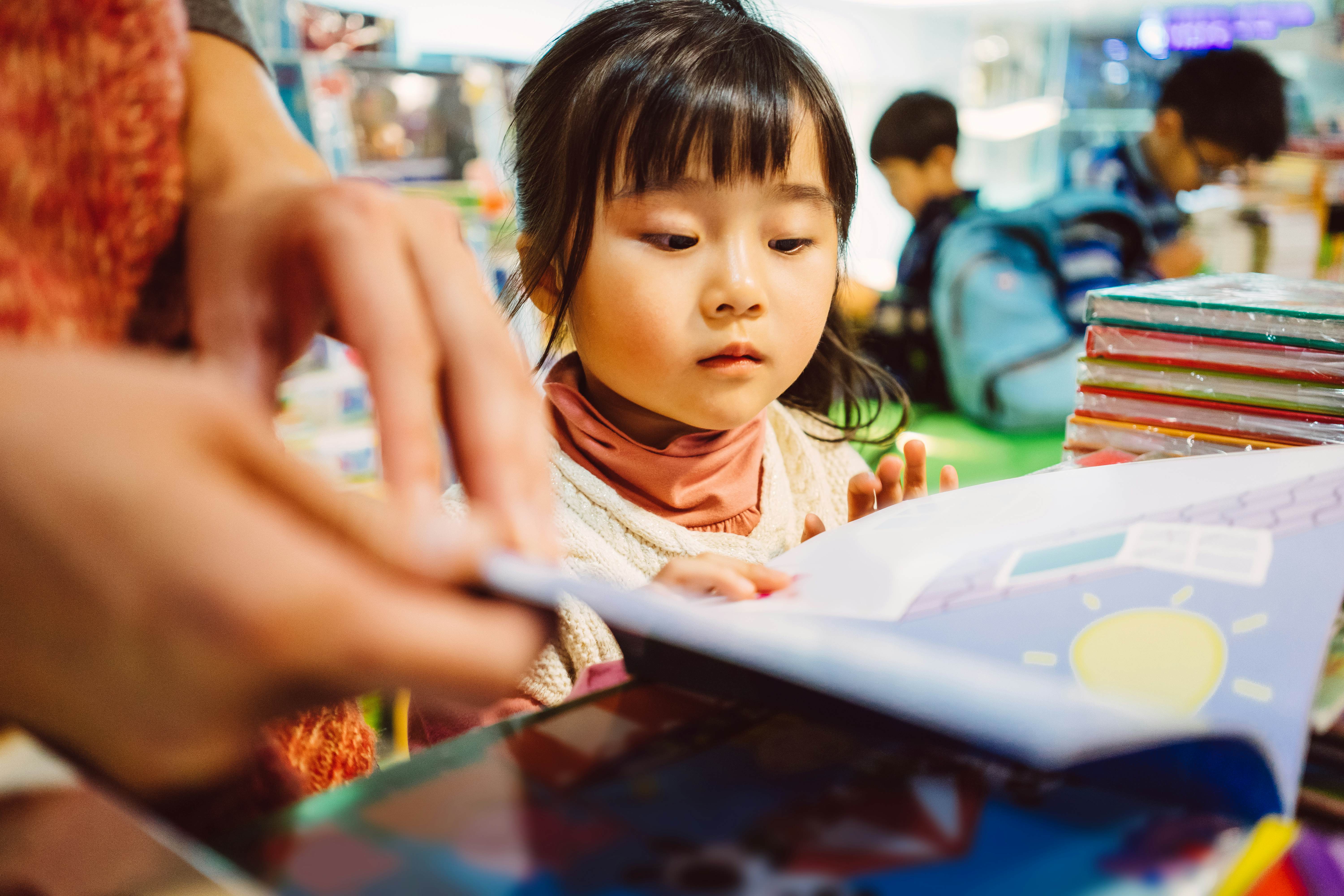 Lovely daughter listening patiently while her mom reading a storybook to her in the bookstore